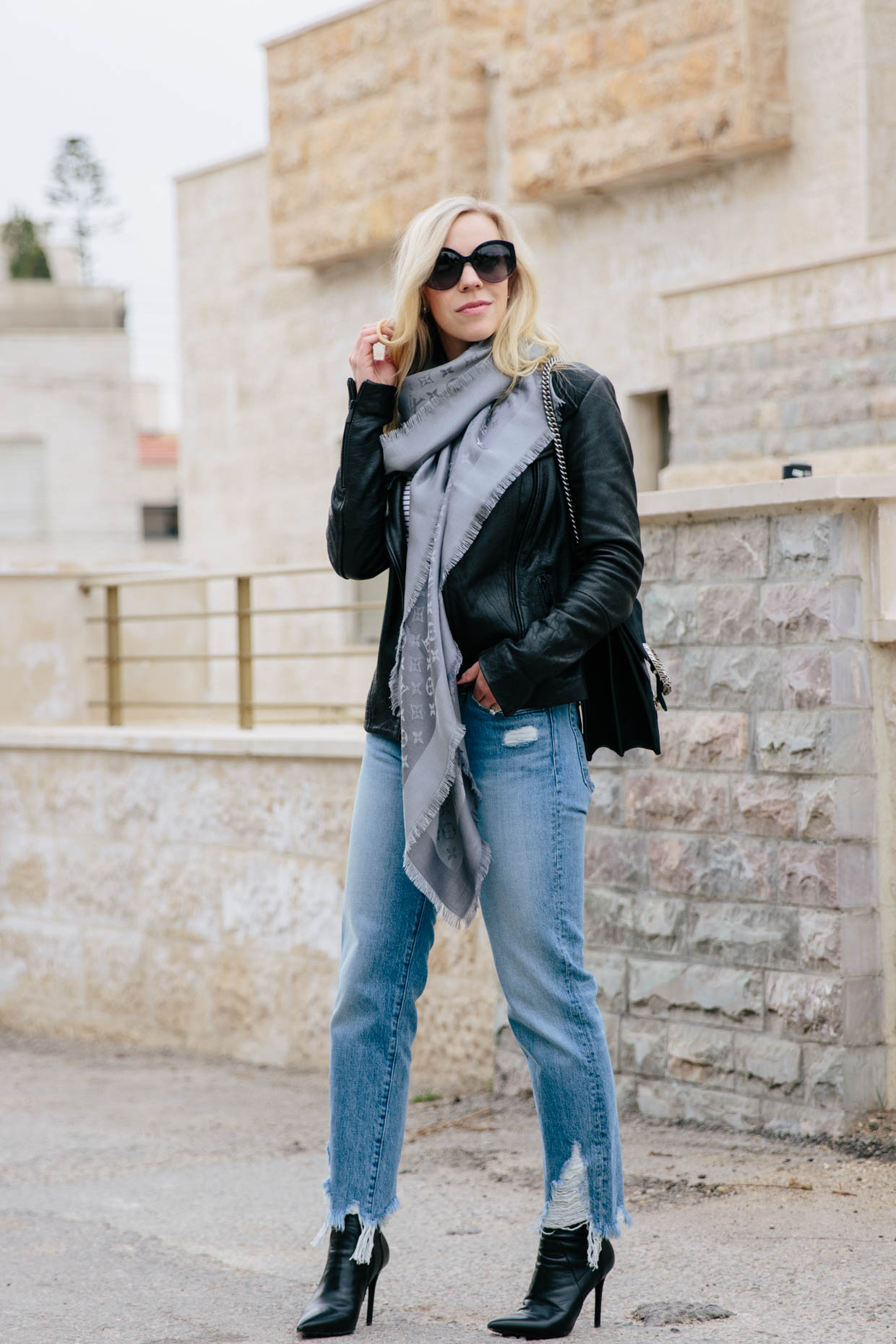Meagan Brandon fashion blogger of Meagan's Moda wears Louis Vuitton black  shine shawl with leather moto jacket, gray high waist jeans and Marc Fisher  black Chelsea boots black and gray outfit 