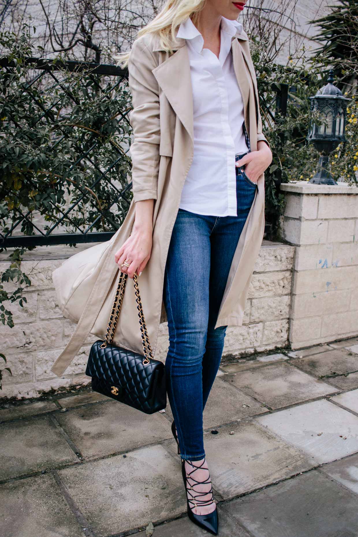 Meagan Brandon fashion blogger of Meagan's Moda styles a khaki trench coat  with white button down shirt and dark blue high waist jeans for classic  khaki trench coat outfit idea - Meagan's