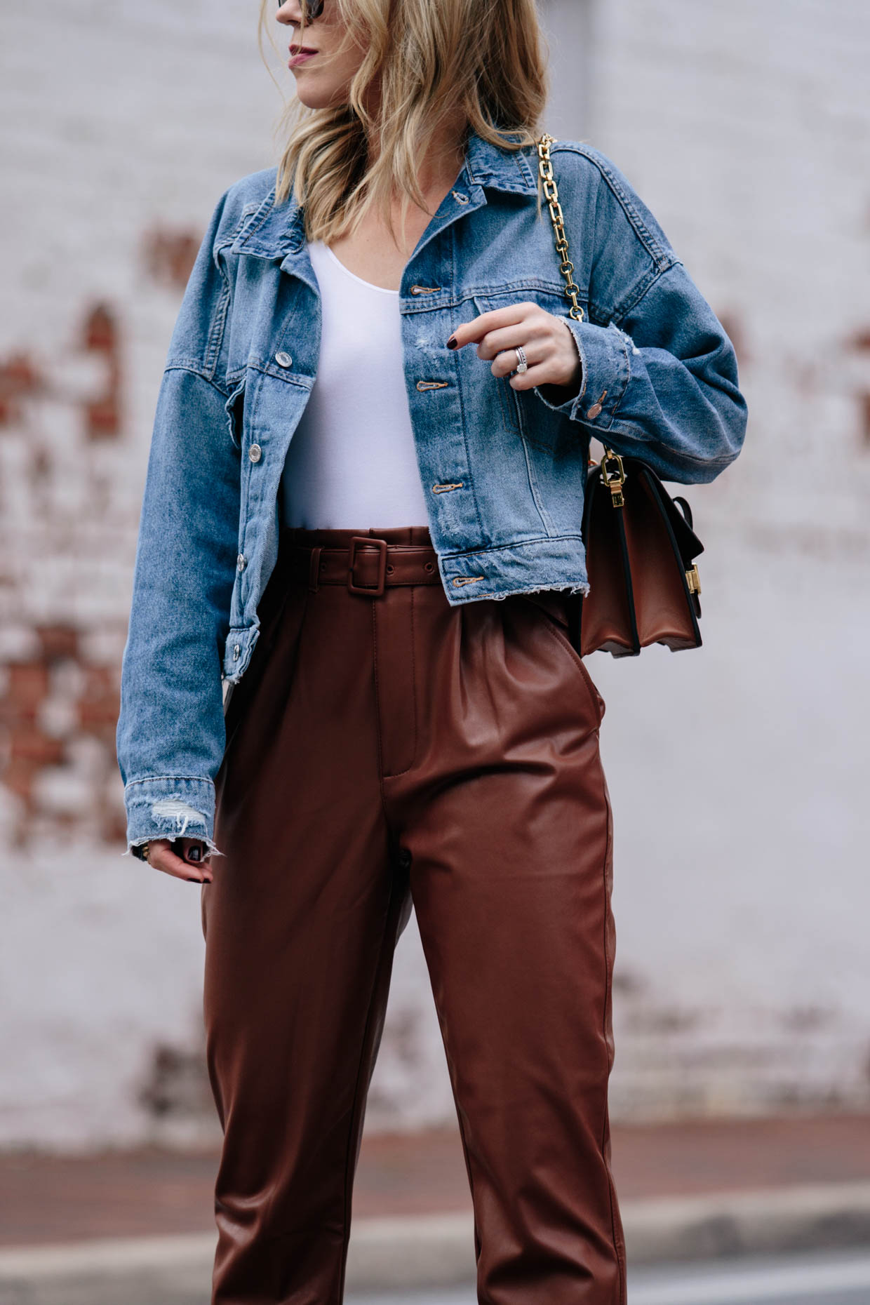 Meagan Brandon fashion blogger of Meagan's Moda wears boxy cropped denim  jacket with white bodysuit, brown faux leather pants and Louis Vuitton Dauphine  bag - Meagan's Moda